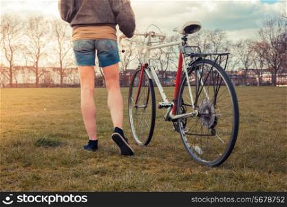 A young woman is walking on the grass in the park with her bicycle