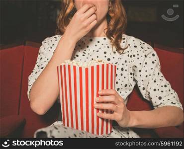A young woman is watching a movie and is eating popcorn at the cinema