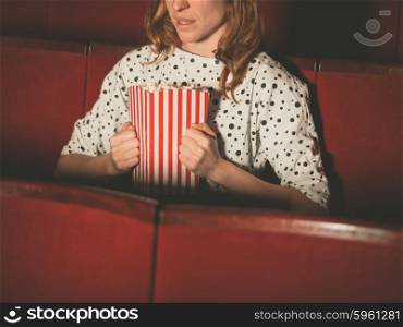 A young woman is watching a suspense movie at the cinema and is clutching her popcorn