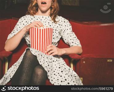 A young woman is watching an exciting movie and is eating popcorn at the cinema