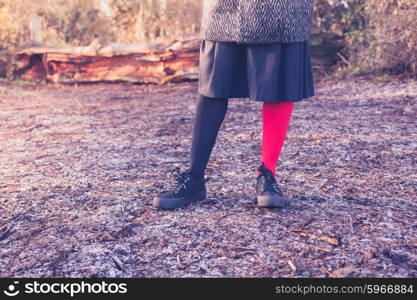 A young woman is wearing odd leggings and is standing on the frosty ground in a forest on a winter day