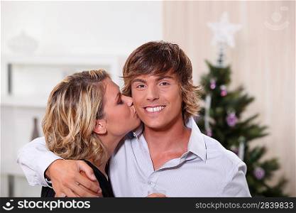 a young woman kissing a young man in front of a Christmas tree