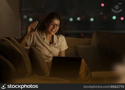 A YOUNG WOMAN LAUGHING WHILE VIDEO CONFERENCING AT NIGHT