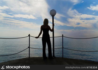 A young woman looking out to sea shot in silhouette against a dramatic early morning sky