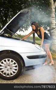 A young woman, looking under the hood of her car to see what&rsquo;s wrong with her engine
