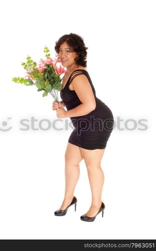 A young woman of mixed race in a black dress standing in profile forwhite background holding a bouquet of flowers.