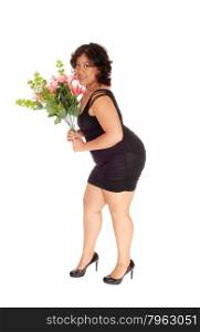 A young woman of mixed race in a black dress standing in profile forwhite background holding a bouquet of flowers.