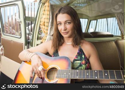 A young woman poses with her guitar in the backseet of her combi van.