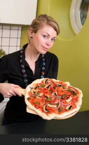 A young woman presents a homemade italian style pizza fresh from the oven in her apartment kitchen.