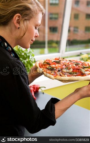 A young woman presents a homemade italian style pizza fresh from the oven in her apartment kitchen.