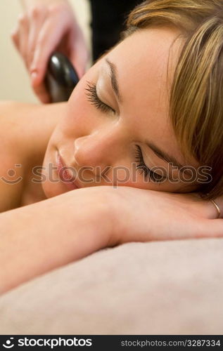 A young woman relaxing at a health spa while having a hot stone massage