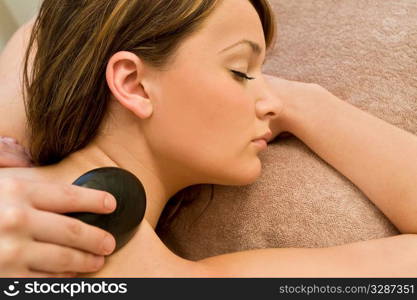 A young woman relaxing at a health spa while having a hot stone massage