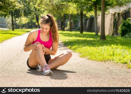 a young woman runner touching knee in pain outdoors