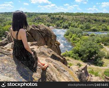 A young woman sits on a rock and looks at a picturesque landscape of the southern bug river. Bug Guard national nature park in Ukraine. Stock photography.. A young woman sits on a rock and looks at a picturesque landscape of the southern bug river. Bug Guard national nature park in Ukraine. Stock photo.