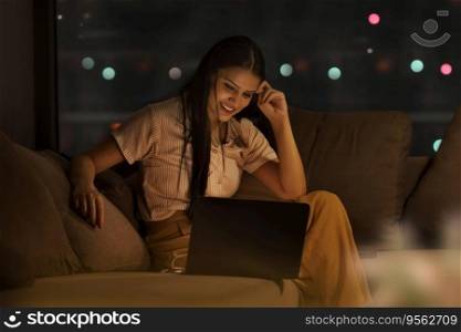 A YOUNG WOMAN SITTING AND USING LAPTOP AT NIGHT
