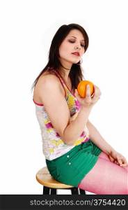 A young woman sitting in green shorts and burgundy pantyhose on a chairholding a yellow orange in her hand, isolated for white background.