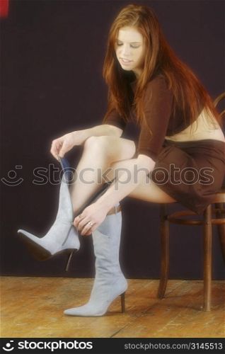 A young woman sitting on chair puts her boot on her foot.