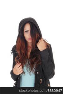A young woman standing in a turquoise t-shirt and black jacket with ahoody, covering halve her face with her hair, over white background
