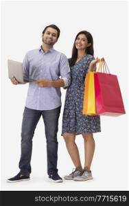 A young woman standing with shopping bags beside a man holding a laptop.