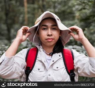A young woman traveler with backpack holding hat and looking at camera, stands in the forest. Travel and relaxation concept.