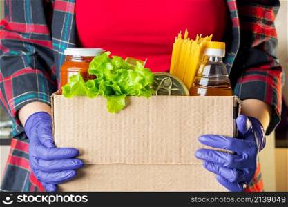 A young woman volunteer is holding a donation box with foodstuffs. Delivery of necessary food during an epidemic.. A woman volunteer is holding a donation box with foodstuffs. Delivery of necessary food during an epidemic.
