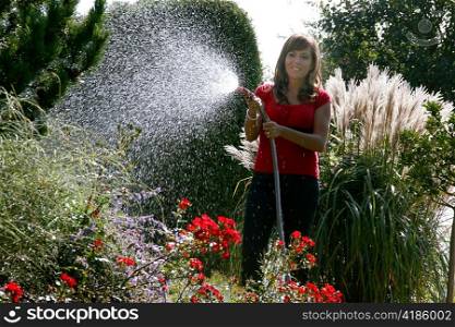 a young woman watering plants in her garden with a garden hose