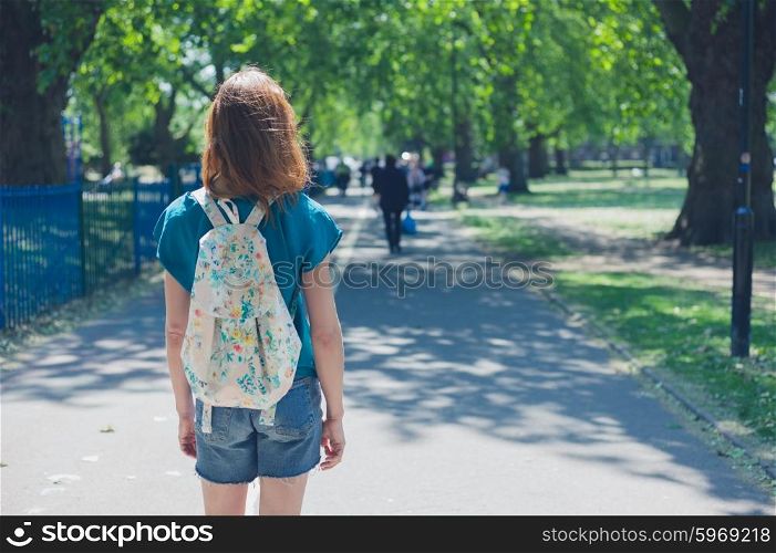 A young woman wearing a bacpack is standig on a path in the park on a summer day