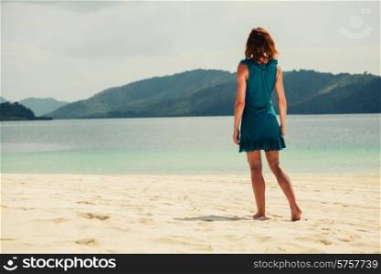 A young woman wearing a blue dress is walking on a tropical beach