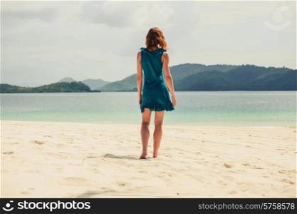 A young woman wearing a blue dress is walking on a tropical beach