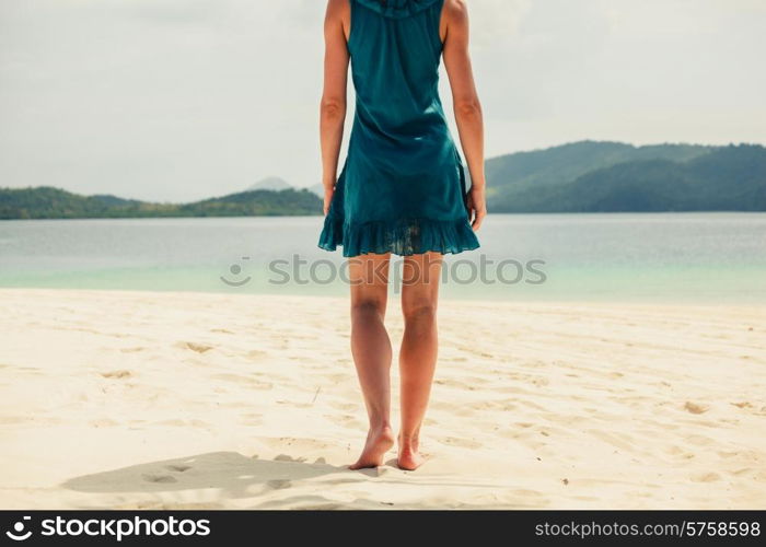 A young woman wearing a blue dress is walking on a tropical beach