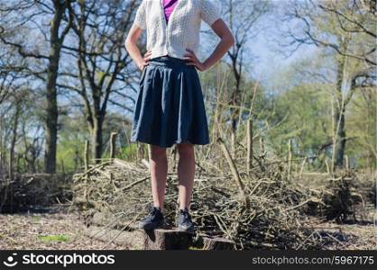 A young woman wearing a blue skirt is standing on a tree trunk in the forest on a sunny spring day