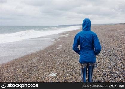 A young woman wearing a blue waterproof jacket is walking on the beach on a cold day