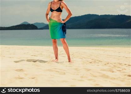 A young woman wearing a colorful sarong is standing on a tropical beach