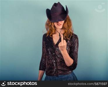 A young woman wearing a cowboy hat is displaying a rude gesture with her middle finger