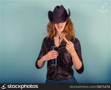 A young woman wearing a cowboy hat is drinking from a beer can and displaying rude gesture