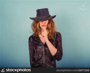 A young woman wearing a cowboy hat is gesturing hush by putting her finger on her lips