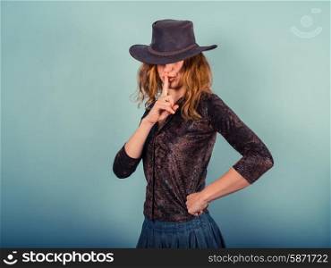 A young woman wearing a cowboy hat is gesturing hush by putting her finger on her lips