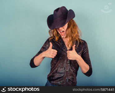 A young woman wearing a cowboy hat is giving two thumbs up