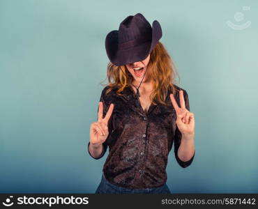A young woman wearing a cowboy hat is showing the peace sign with her hands