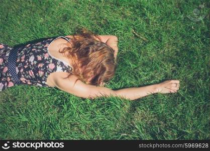A young woman wearing a dress is lying in the green grass on a sunny summer day