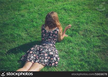 A young woman wearing a dress is lying in the green grass on a sunny summer day