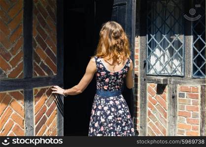 A young woman wearing a dress is opening a door and is entering an old rustic farmhouse in the summer
