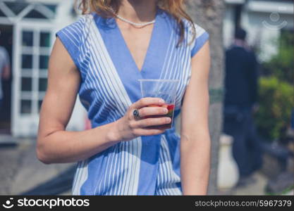 A young woman wearing a dress is relaxing with a drink in a garden on a sunny summer day