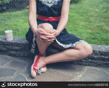 A young woman wearing a dress is sitting in a garden with a cup of tea