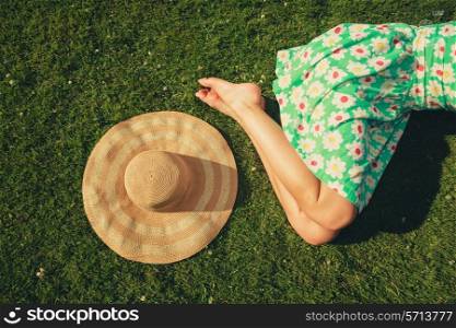 A young woman wearing a dress is sleeping on the grass with a hat next to her