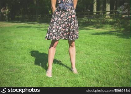 A young woman wearing a dress is standing in a field near a fence on a summer day