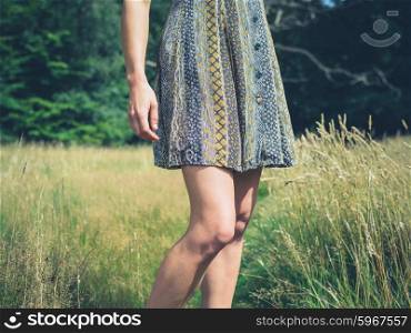 A young woman wearing a dress is standing in a meadow by a forest