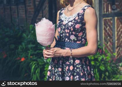 A young woman wearing a dress is standing outside an old farmhouse with a candyfloss on a sunny summer day