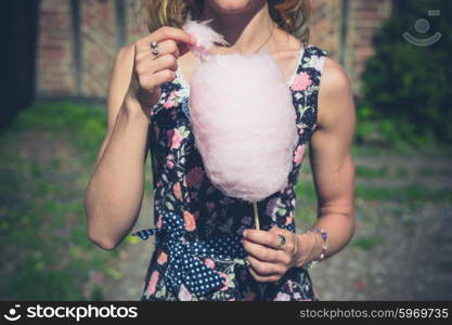 A young woman wearing a dress is standing outside an old farmhouse with a candyfloss on a sunny summer day