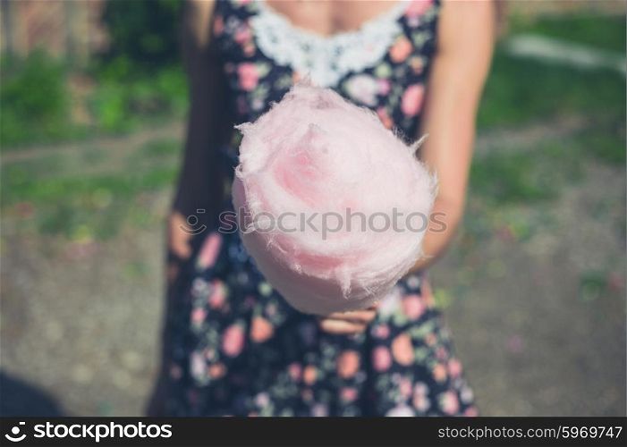 A young woman wearing a dress is standing outside with a candyfloss on a sunny summer day